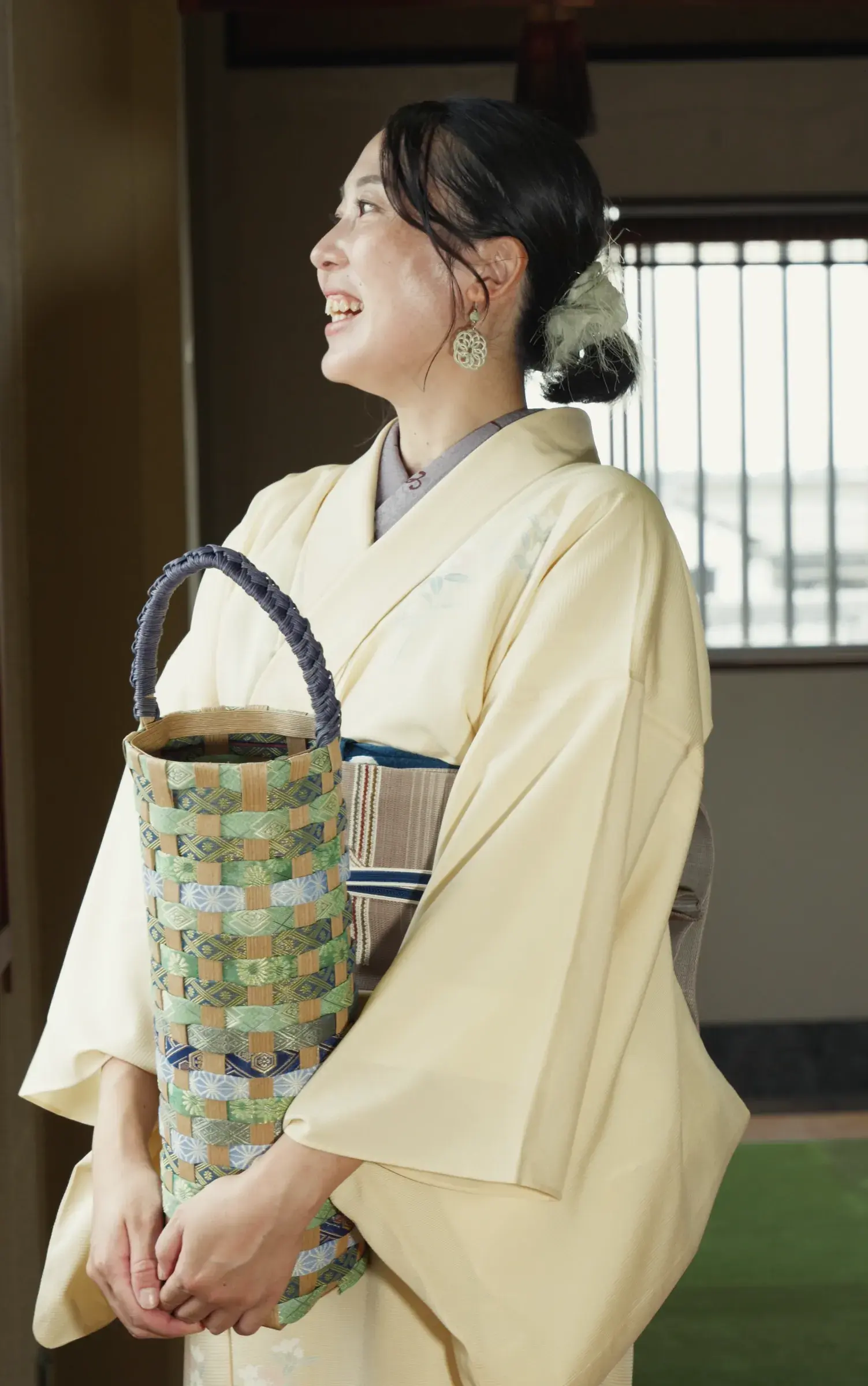 Laughing, a tall bottle bag of green and sky-blue tatami-beri held at the waist